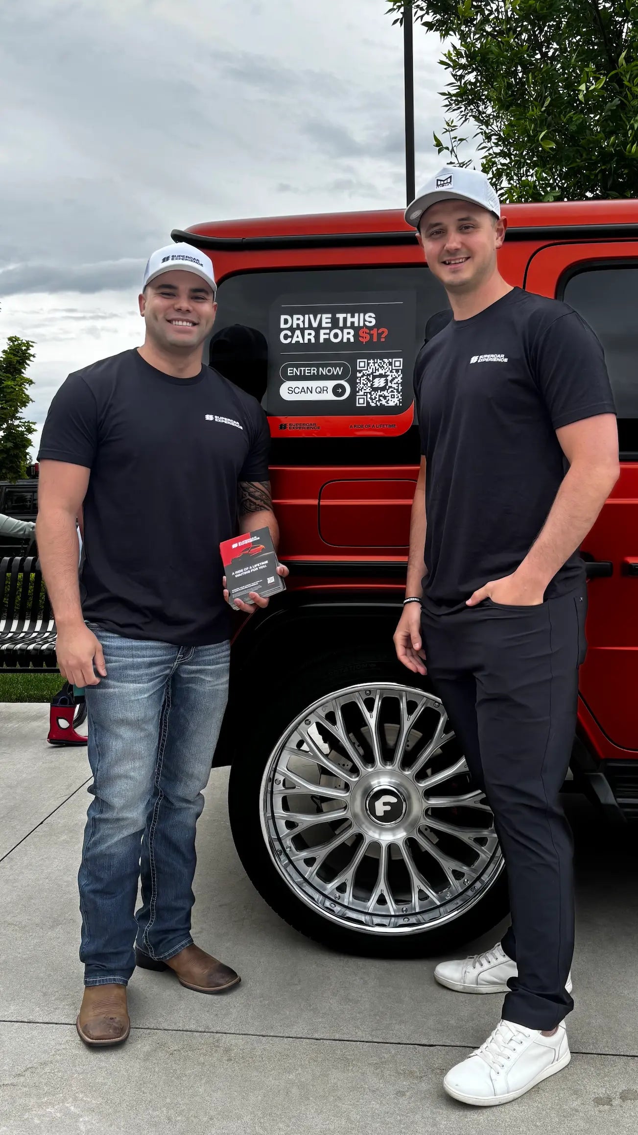 2 people standing next to mercedes with supercar marketing materials
